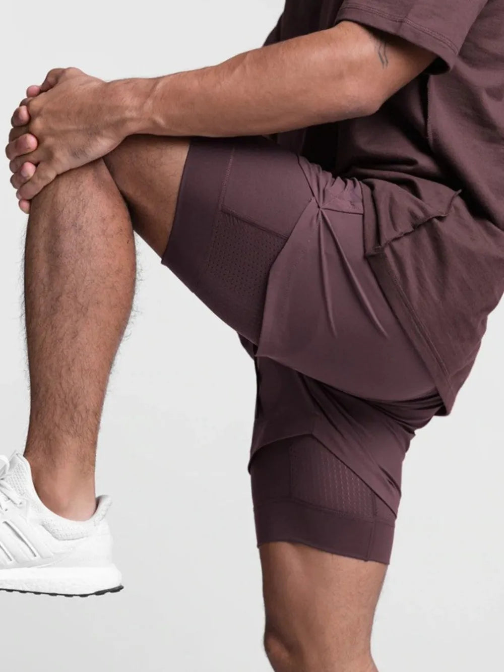 Trendsi active shorts for men in dark brown worn by a man stretching with white sneakers